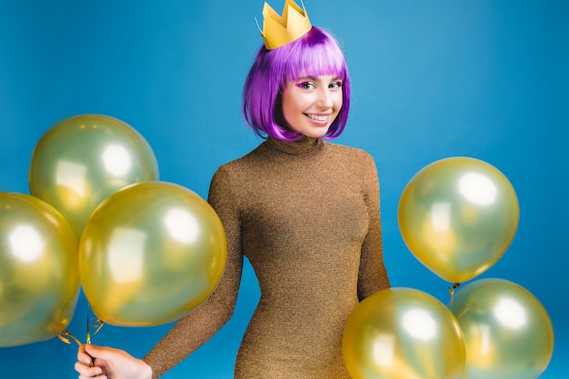 Momentos de celebración feliz de mujer joven sonriente divirtiéndose con globos dorados. Vestido de moda de lujo, corte de pelo morado, corona, celebración, fiesta de año nuevo, cumpleaños.