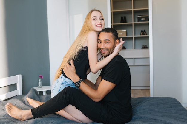 Momentos de la encantadora pareja de chico guapo y joven mujer bonita con cabello largo rubio sonriendo. Relajarse en la cama en casa en un apartamento moderno, relación, verdaderas emociones, enamorado