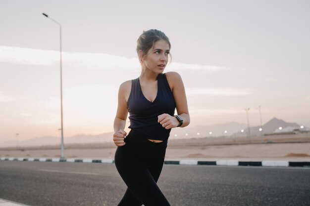 Momentos felices de la mañana soleada de trabajadora motivada increíble joven en ropa deportiva corriendo en la carretera en un país tropical temprano en la mañana. Entrenamiento, entrenamiento, estilo de vida saludable