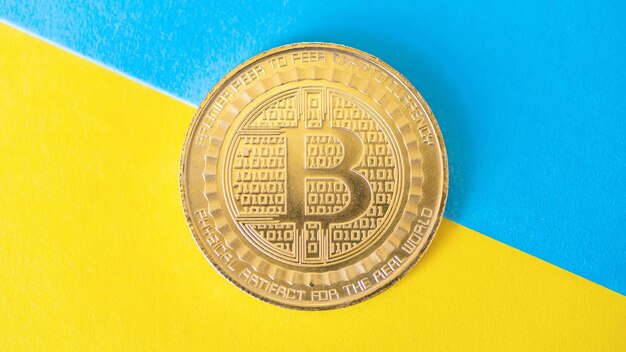 Moneda de oro Bitcoin física fondo azul y amarillo