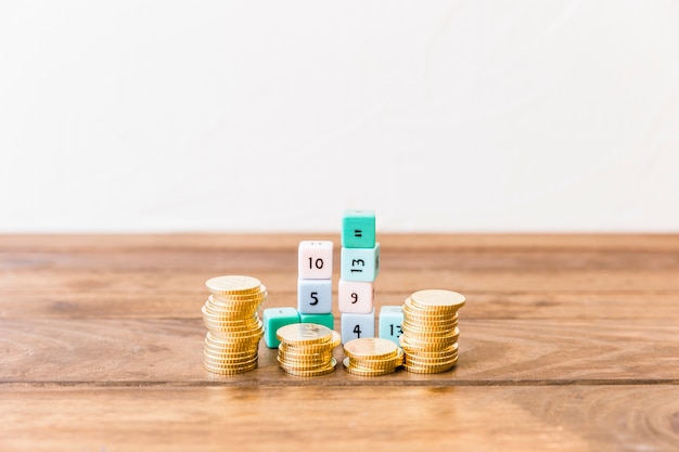 Monedas apiladas y bloques de matemáticas en la mesa de madera