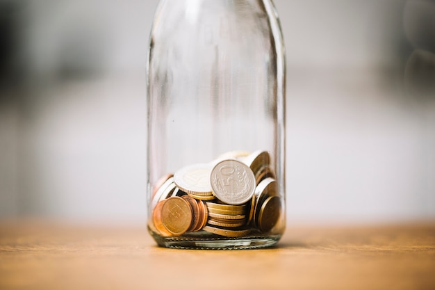 Foto gratuita monedas en la botella de vidrio en la superficie de madera