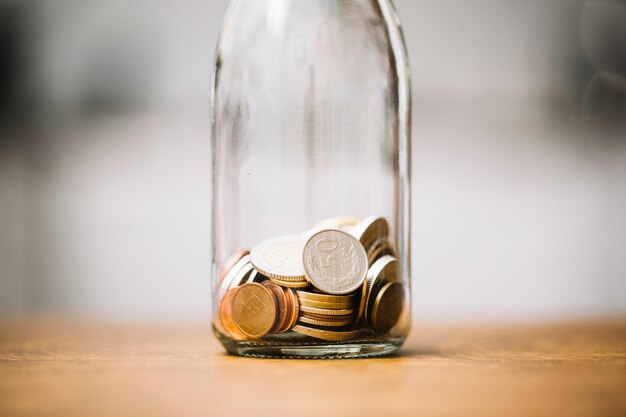 Monedas en la botella de vidrio en la superficie de madera