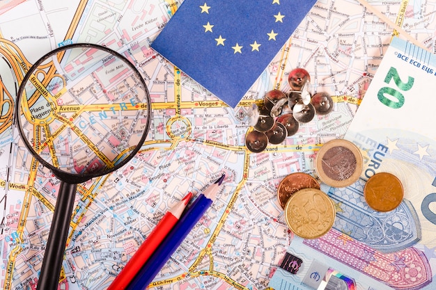 Monedas del euro con lupa, marcadores, lápices y bandera en el mapa mundial