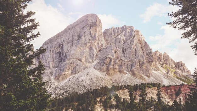 Montaña marrón cerca de árboles verdes bajo el cielo nublado soleado blanco y azul