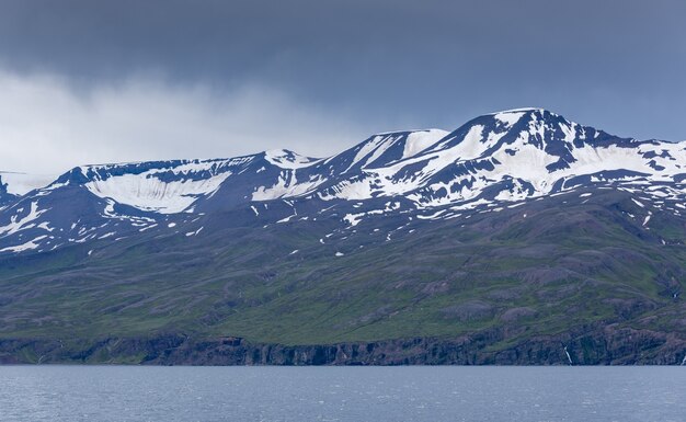 Montañas con fotos nevadas cerca del mar en un día sombrío en Islandia