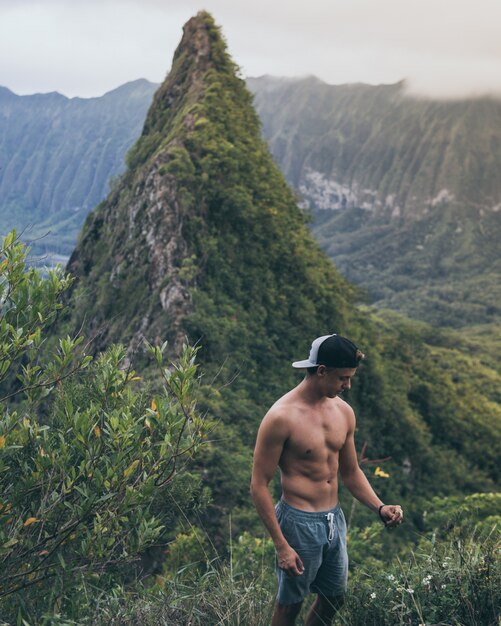 Montar excursionista masculino en una gorra en blanco y negro de pie en medio de los campos de hierba en Hawai