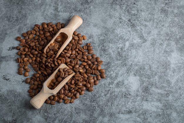 Montón de aromáticos granos de café y cucharas de madera sobre fondo de mármol