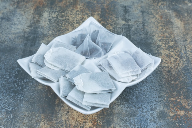 Montón de bolsitas de té negro en un plato blanco.