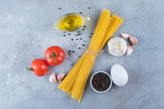 Montón de espaguetis crudos en cuerda con tomates rojos frescos y ajo.