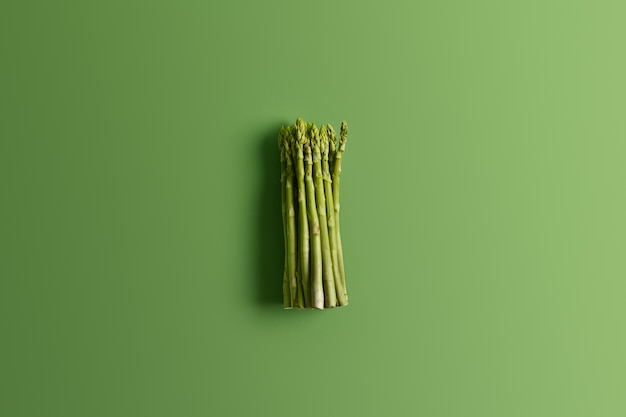 Foto gratuita montón de espárragos frescos sobre fondo verde vivo. ingrediente para preparar una deliciosa ensalada vegetariana. concepto de comida. verduras frescas de primavera. brotes comestibles de espárragos ricos en vitaminas, ácido fólico
