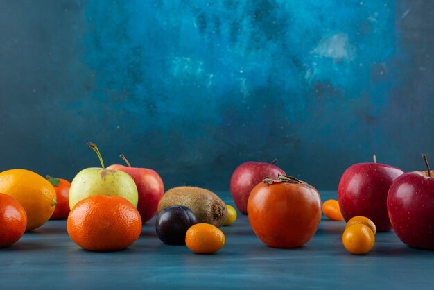 Montón de frutas frescas enteras colocadas sobre una superficie azul.