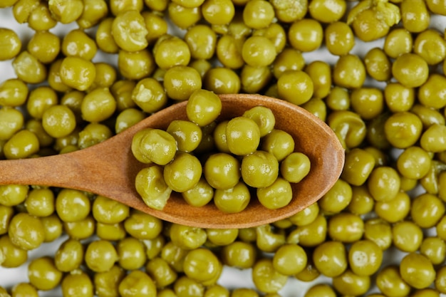 Un montón de guisantes hervidos con una cuchara de madera sobre una mesa blanca.