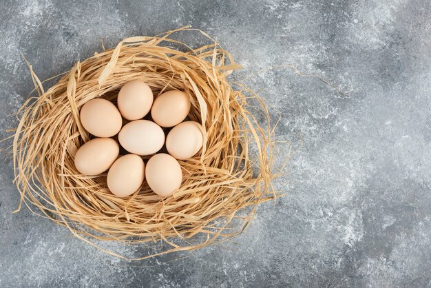 Montón de huevos crudos con nido de pájaro sobre superficie de mármol.