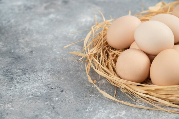 Montón de huevos crudos con nido de pájaro sobre superficie de mármol.