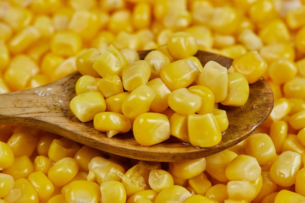 Un montón de maíz dulce hervido con una cuchara de madera sobre una mesa blanca.