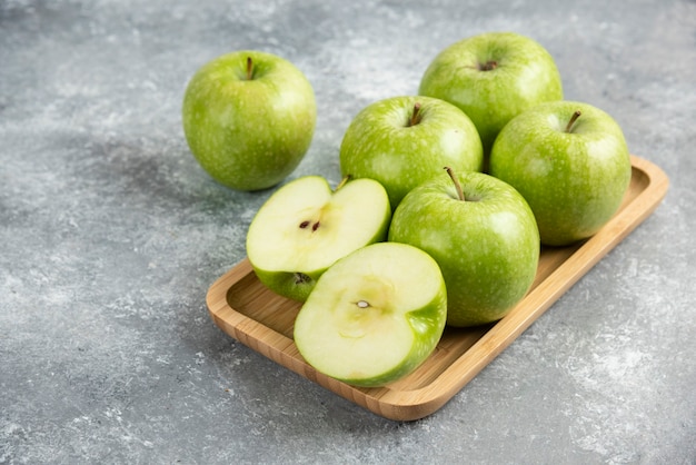 Montón de manzanas verdes enteras y en rodajas sobre placa de madera.