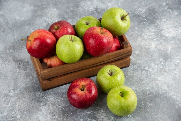 Montón de manzanas verdes y rojas frescas colocadas en caja de madera.