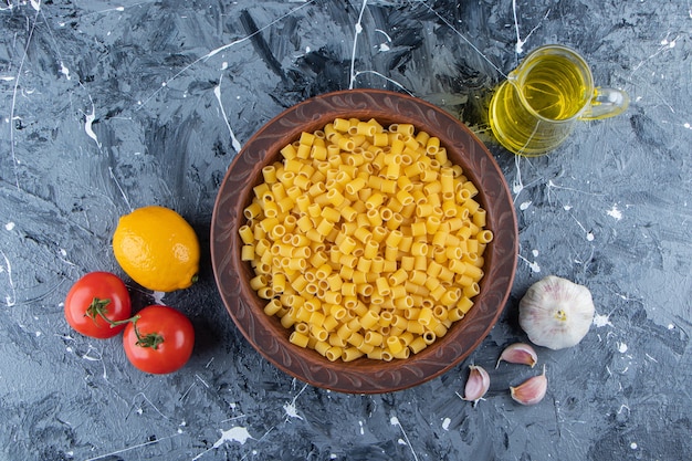 Montón de pasta cruda pipeta rigate en un recipiente con tomates rojos frescos y aceite.