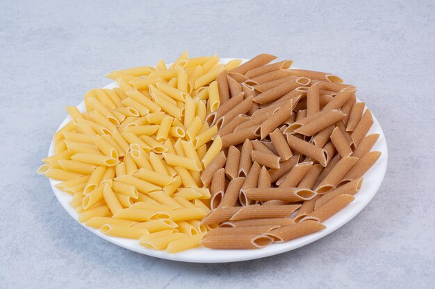 Montón de pasta penne marrón y amarillo en la placa blanca.