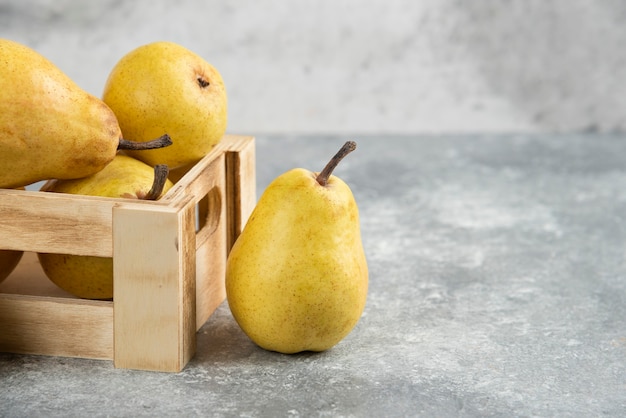 Montón de peras bio frescas en caja de madera sobre superficie de mármol.