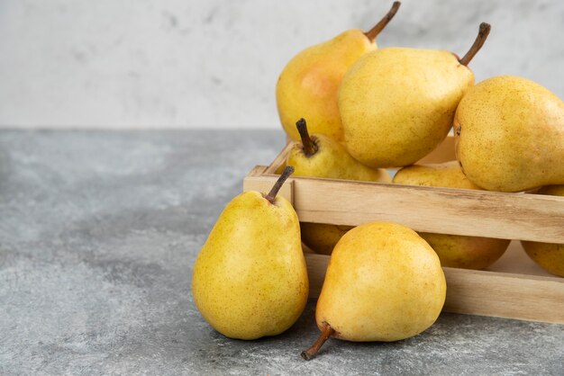 Montón de peras bio frescas en caja de madera sobre superficie de mármol.