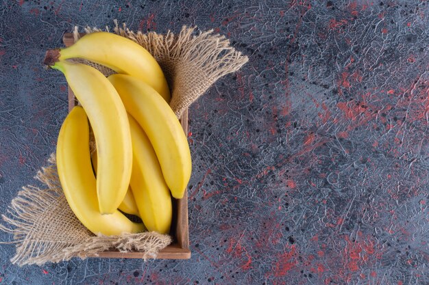 Montón de plátano fresco en caja de madera en superficie colorida