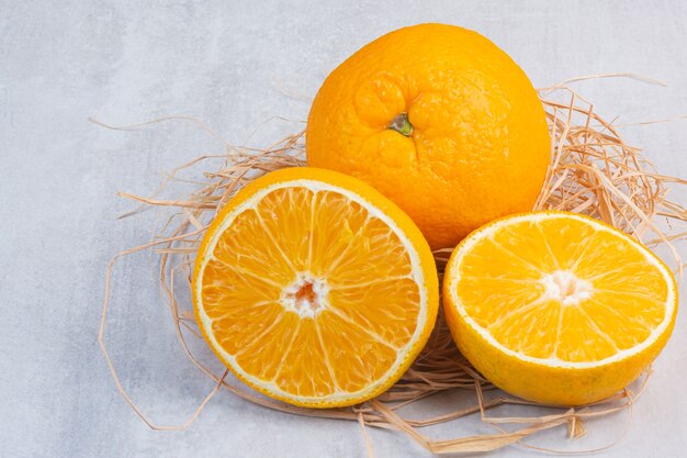 Un montón de sabrosas naranjas sobre una pajita, sobre la mesa de mármol.