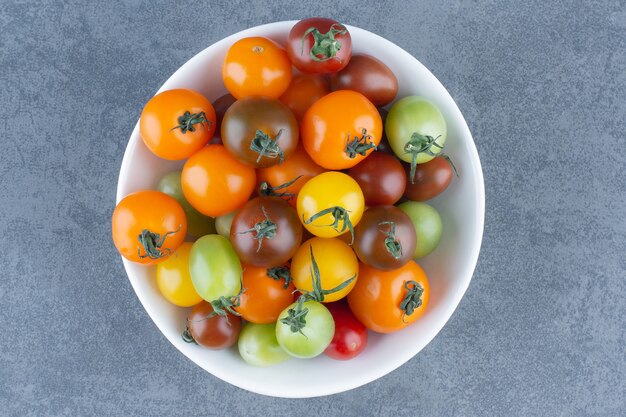 Montón de tomates coloridos en tazón de fuente blanco.