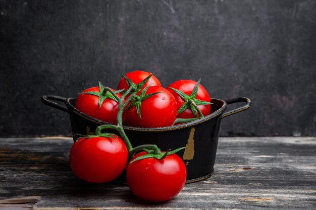 Un montón de tomates en una olla sobre un viejo fondo de madera y negro. vista lateral.