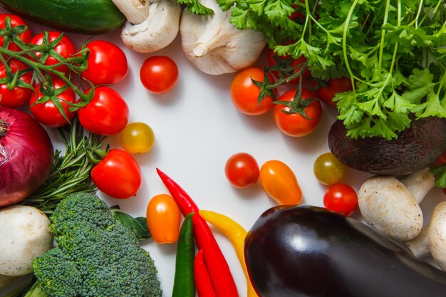 Un montón de tomates con pimientos, brócoli, ajo, champiñones, berenjenas, cebolla vista superior sobre una superficie blanca