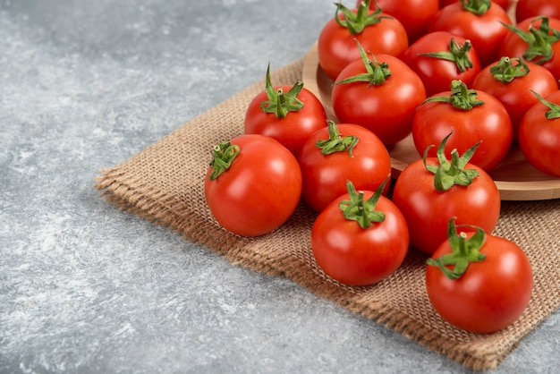 Montón de tomates rojos frescos con tela de saco sobre superficie de mármol.