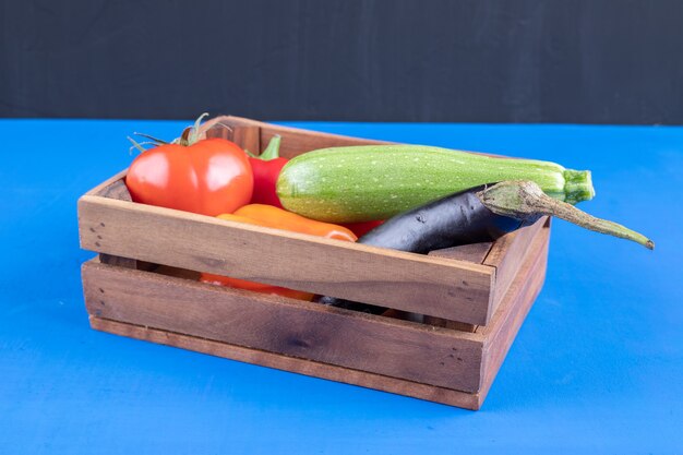 Montón de verduras frescas maduras en caja de madera sobre superficie azul