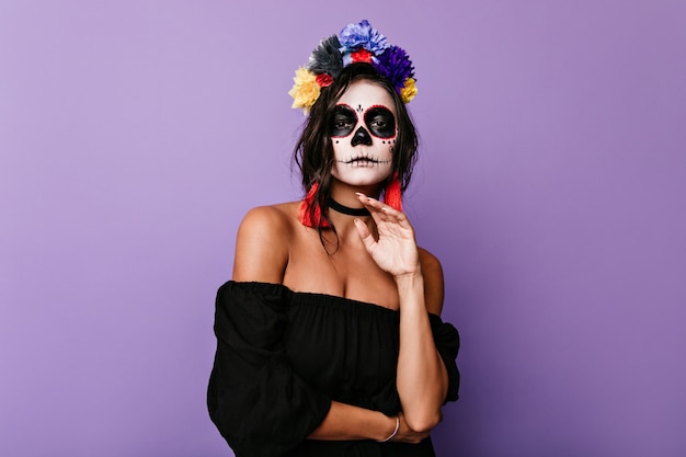 Morena atractiva con poses de máscara mexicana en traje de halloween. Mujer vestida de negro con confianza