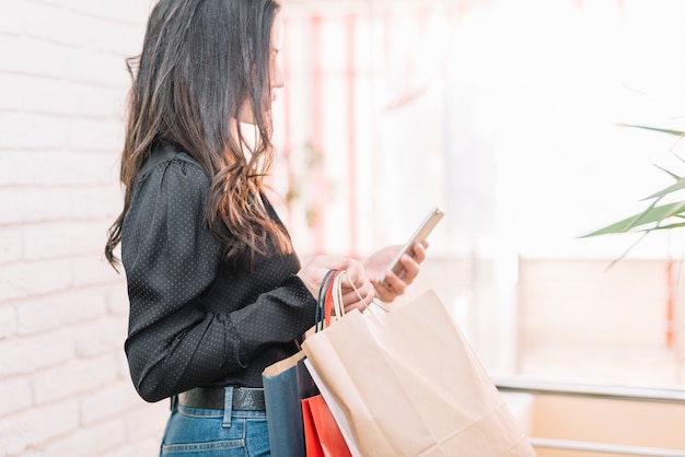 Foto gratuita morena con bolsos y smartphone en luz.