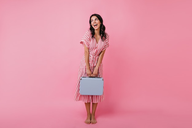 Morena con cabello ondulado es linda posando con vestido midi a rayas. Mujer con traje elegante mira hacia otro lado con interés.