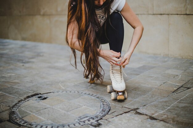 Morena chica agazapado atar rollerskates fuera