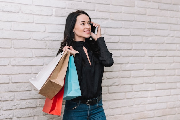 Morena elegante con bolsas charlando por teléfono