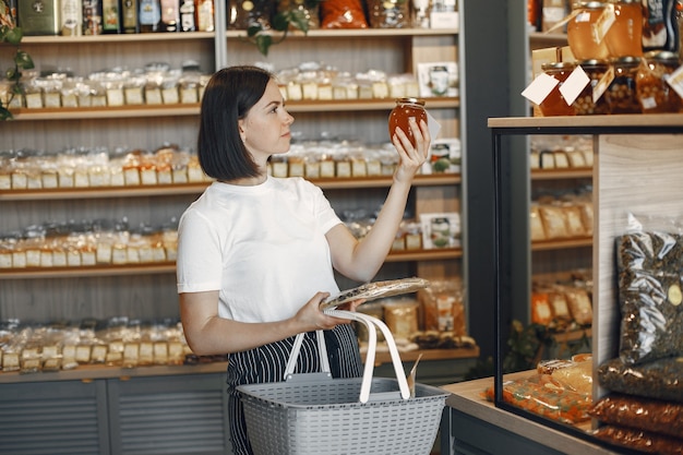 Morena elige comida. Señora está sosteniendo un carrito de compras. Niña con una camisa blanca en el supermercado.