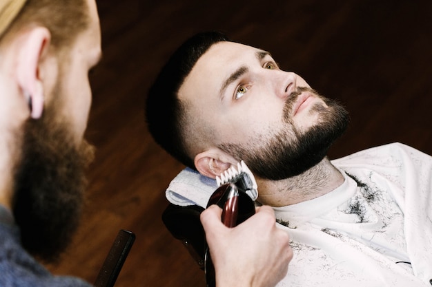 Morena hombre se encuentra con los ojos abiertos mientras barbero corta su barba