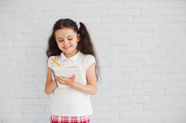 Morena linda chica de pie escribiendo en el bloc de notas con lápiz