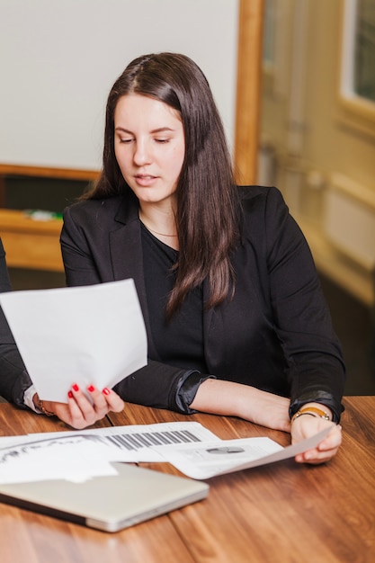 Morena mujer sentada en el escritorio leyendo documentos