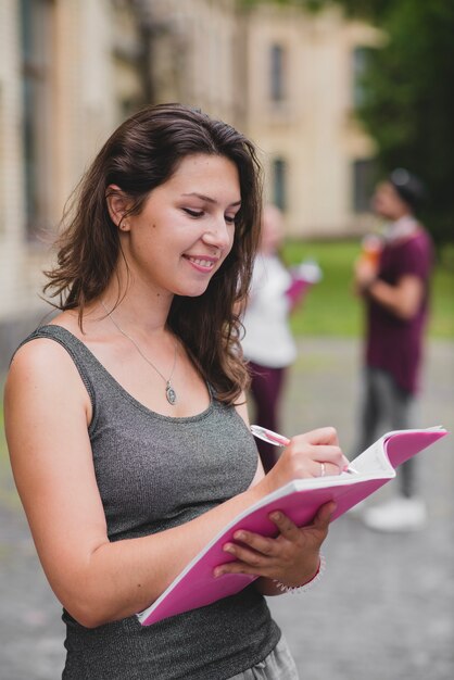 Morena niña de pie la celebración de escribir cuaderno