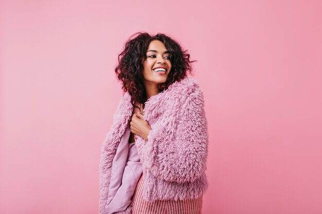 Morena positiva y sonriente en traje rosa mira con alegría a la distancia. Retrato de niña con piel bronceada.