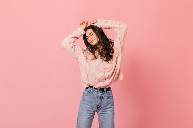 Foto gratuita morena rizada bailando sobre fondo rosa. retrato de niña de buen humor en suéter caliente y jeans de mamá.