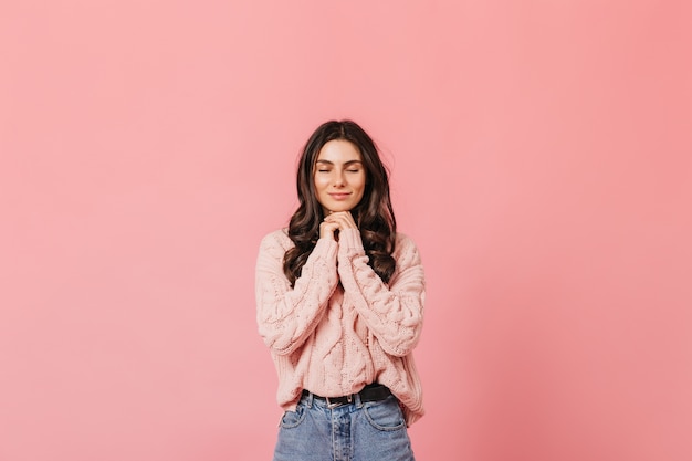 Foto gratuita morena rizada sonríe tranquilamente con los ojos cerrados sobre fondo rosa y pide un deseo.