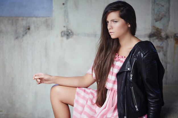 Morena sexy con vestido rosa y chaqueta de cuero posando en la cámara.