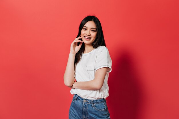 Morena vestida con camiseta y jeans mira al frente en la pared roja