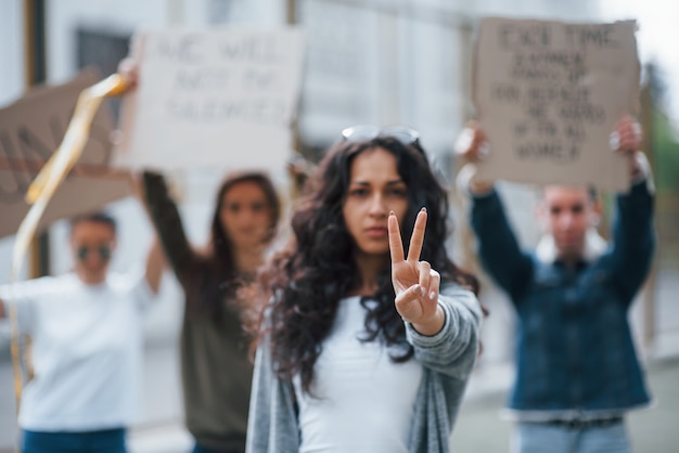 Mostrando gesto con dos dedos. Grupo de mujeres feministas al aire libre protesta por sus derechos