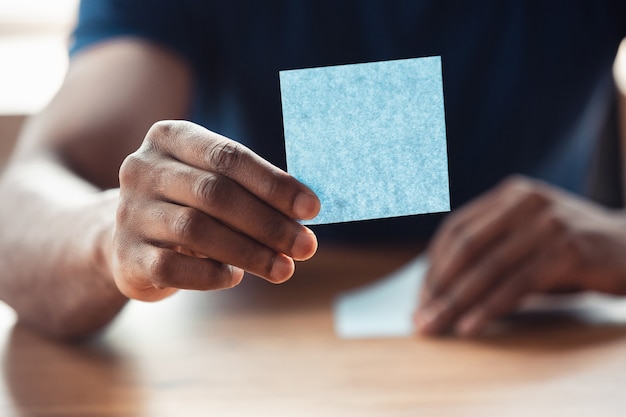 Mostrando pegatinas en blanco. Cerca de manos masculinas afroamericanas, trabajando en la oficina. Concepto de negocio, finanzas, trabajo, compras en línea o ventas. Copyspace para publicidad. Educación, autónomo.